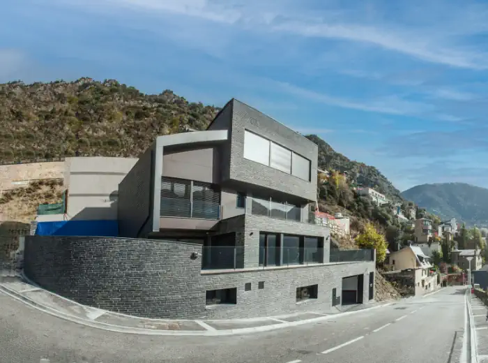Habitatge contemporani construït per Coansa amb arquitectura moderna, façana de pedra i grans finestrals integrats en l’entorn de muntanya.
