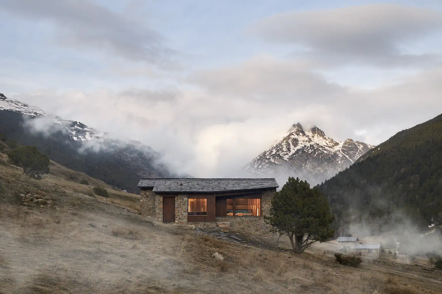 Casa contemporània integrada al paisatge de la Vall d’Incles amb muntanyes nevades al fons i ambient de boira a Andorra.